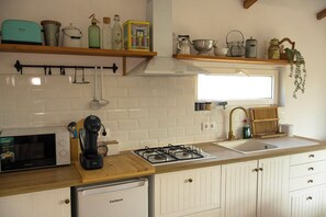 Una cocina con armarios blancos, una estufa a gas, un microondas y diversos utensilios de cocina en estantes.