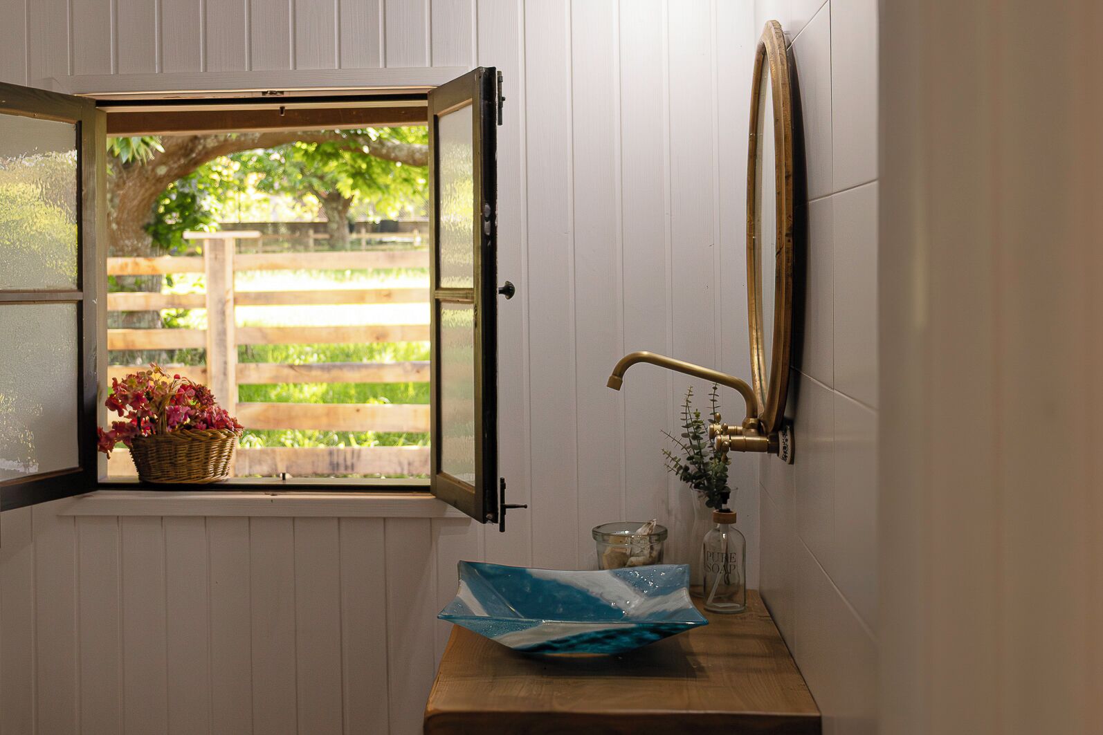 A bathroom with a window, a sink, a mirror, and a basket of flowers.