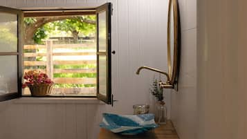 A bathroom with a window, a sink, a mirror, and a basket of flowers.