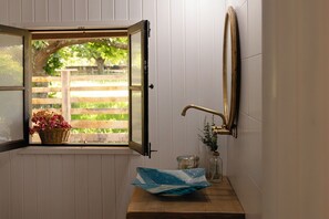 Un baño con ventana, lavamanos, espejo y una cesta de flores.