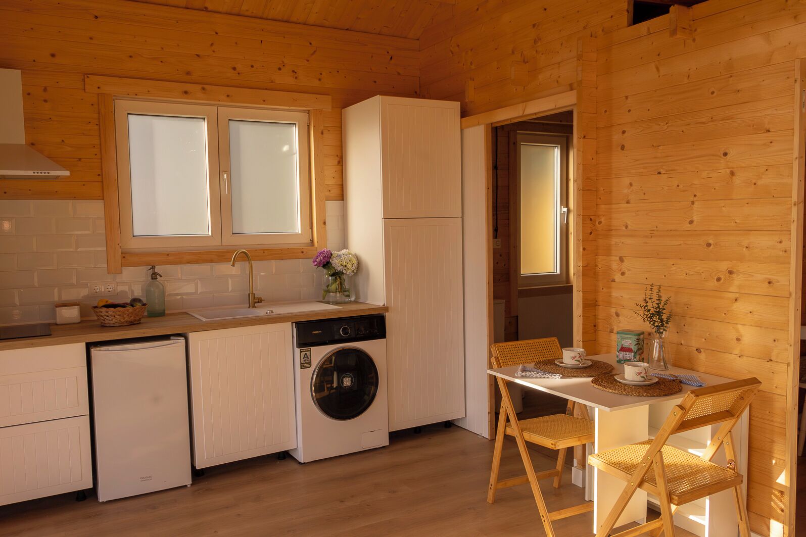A compact kitchen with a washing machine, a sink, and a dining area with a table and chairs.