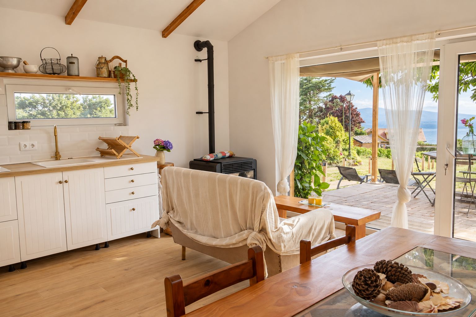Una cocina acogedora con una mesa y sillas de madera, un ventanal con vistas a la vegetación y un comedor con mesa lista para dos.