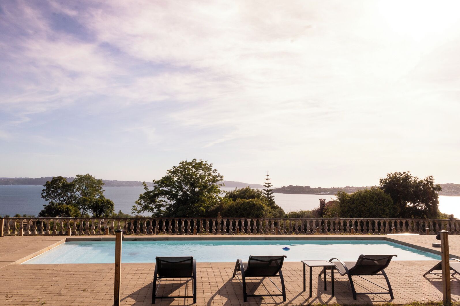 Una piscina con sillones de descanso y vistas al mar.