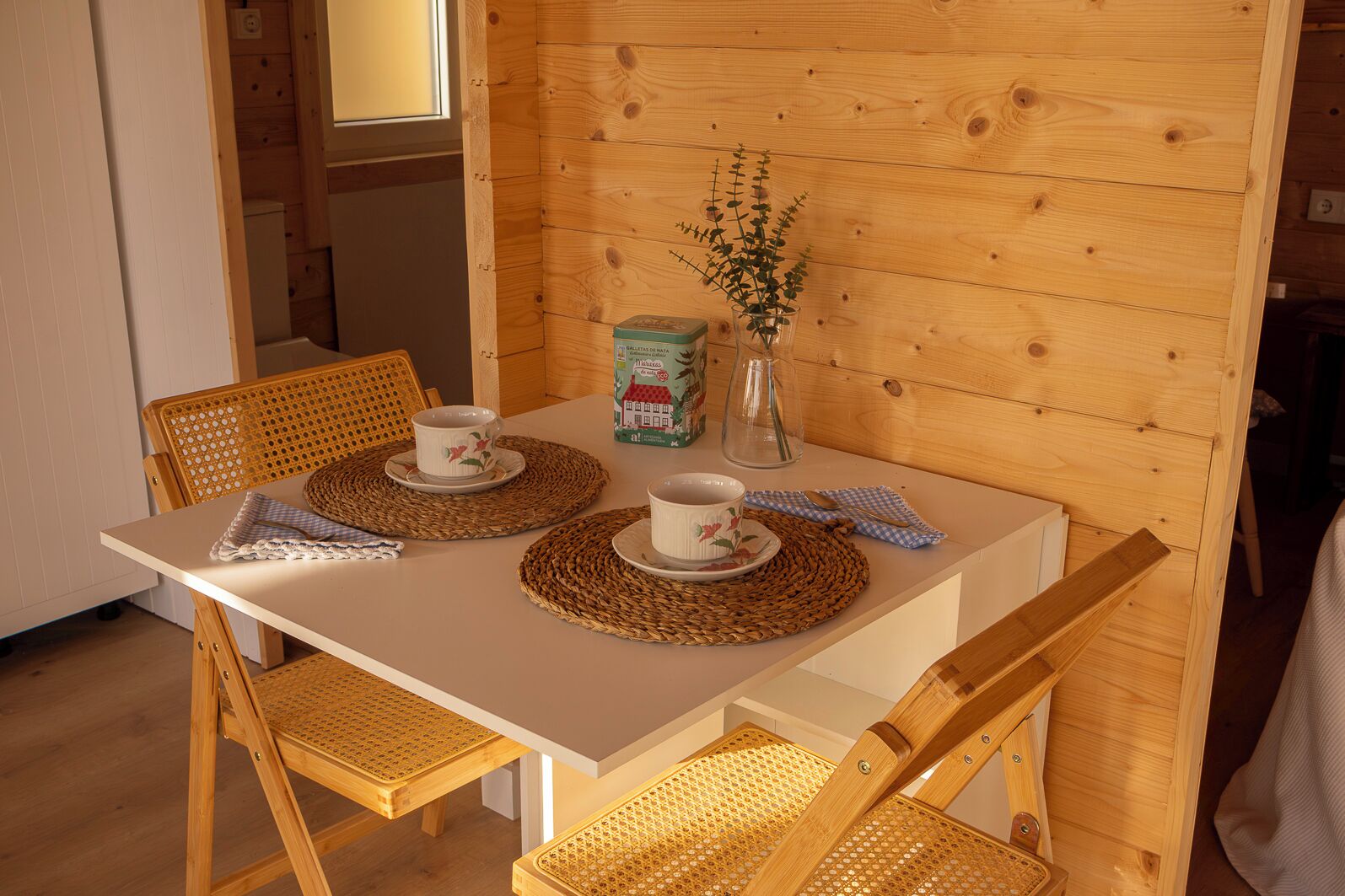Una mesa de madera para comer con dos sillas, un florero con flores y un libro sobre la mesa.