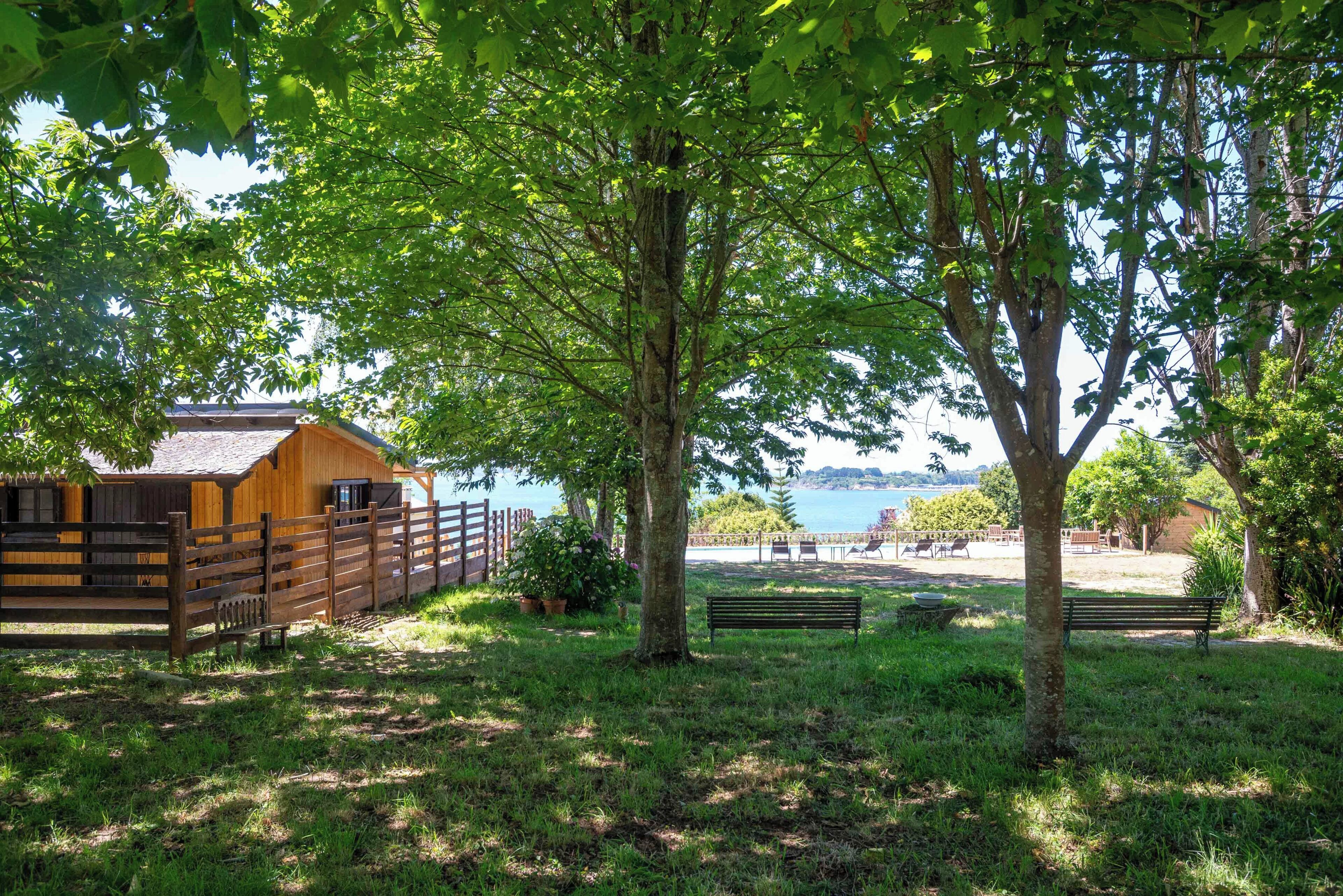 A wooden cabin with a fenced area, a bench, and a view of the sea.