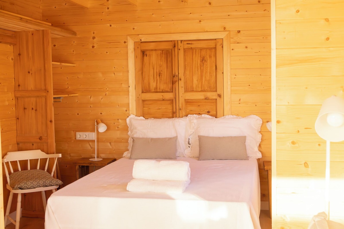 Camera da letto in una baita di legno, con un letto, cuscini, una sedia e una lampada da comodino.