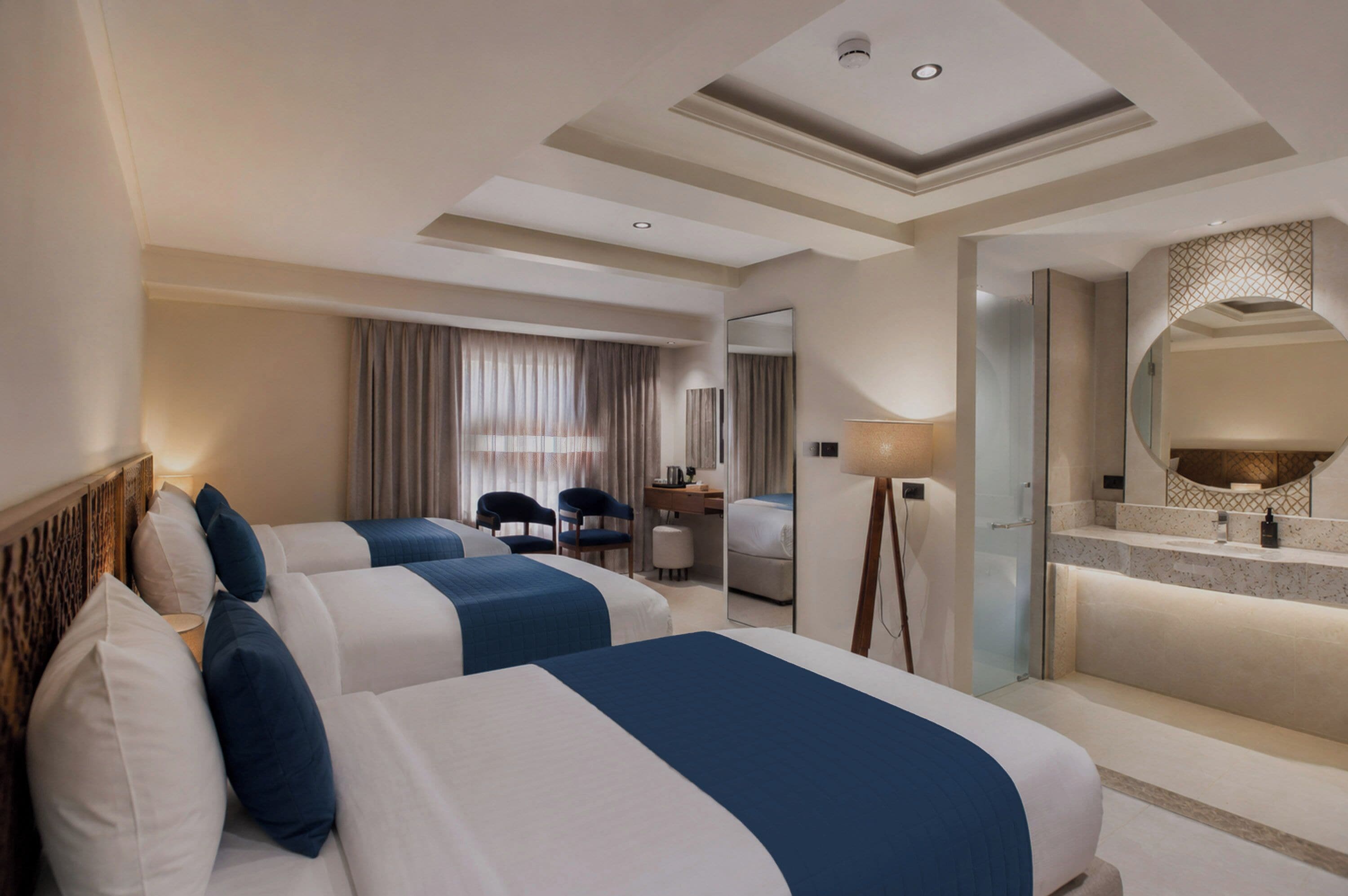 Habitación de hotel con dos camas, un escritorio, una silla, un espejo y un baño con ducha y lavabo.