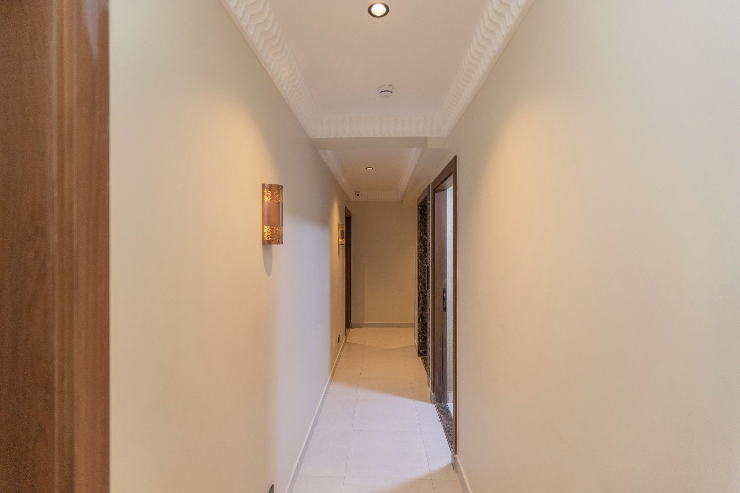 Un couloir étroit, avec une porte en bois sur la gauche, un luminaire fixé au mur et une porte avec un panneau de verre sur la droite.