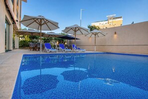 A swimming pool with lounge chairs and umbrellas, surrounded by a building with a flat roof and a clear sky. - Touring Pyramids Hotel (Giza)