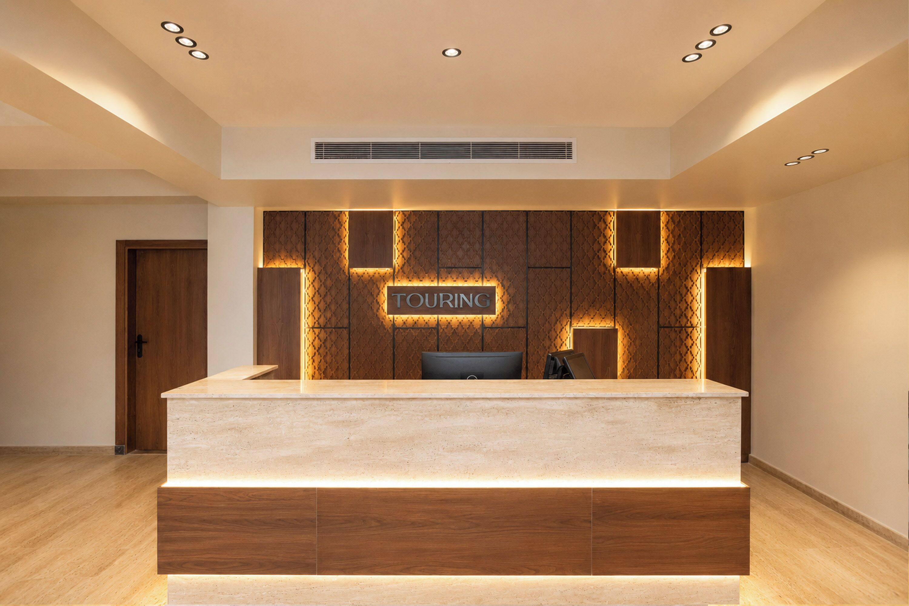 A reception desk with a sign that reads 'TOURING' and a modern, geometric wall design behind it.