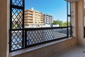 Un balcón con barandilla metálica de diseño geométrico, vista a un edificio de varios pisos con balcones y un cielo despejado.