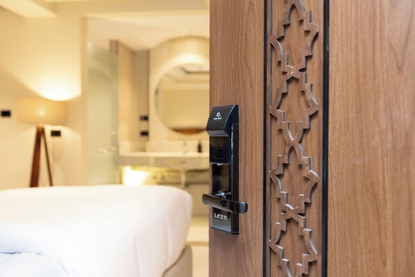 A hotel room with a bed, a wooden door with a card reader, and a mirror. - Touring Pyramids Hotel (Giza)