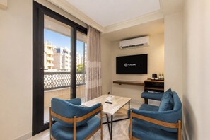 Una habitación de hotel moderna con balcón, televisor de pantalla plana, una mesita y dos sillas azules.