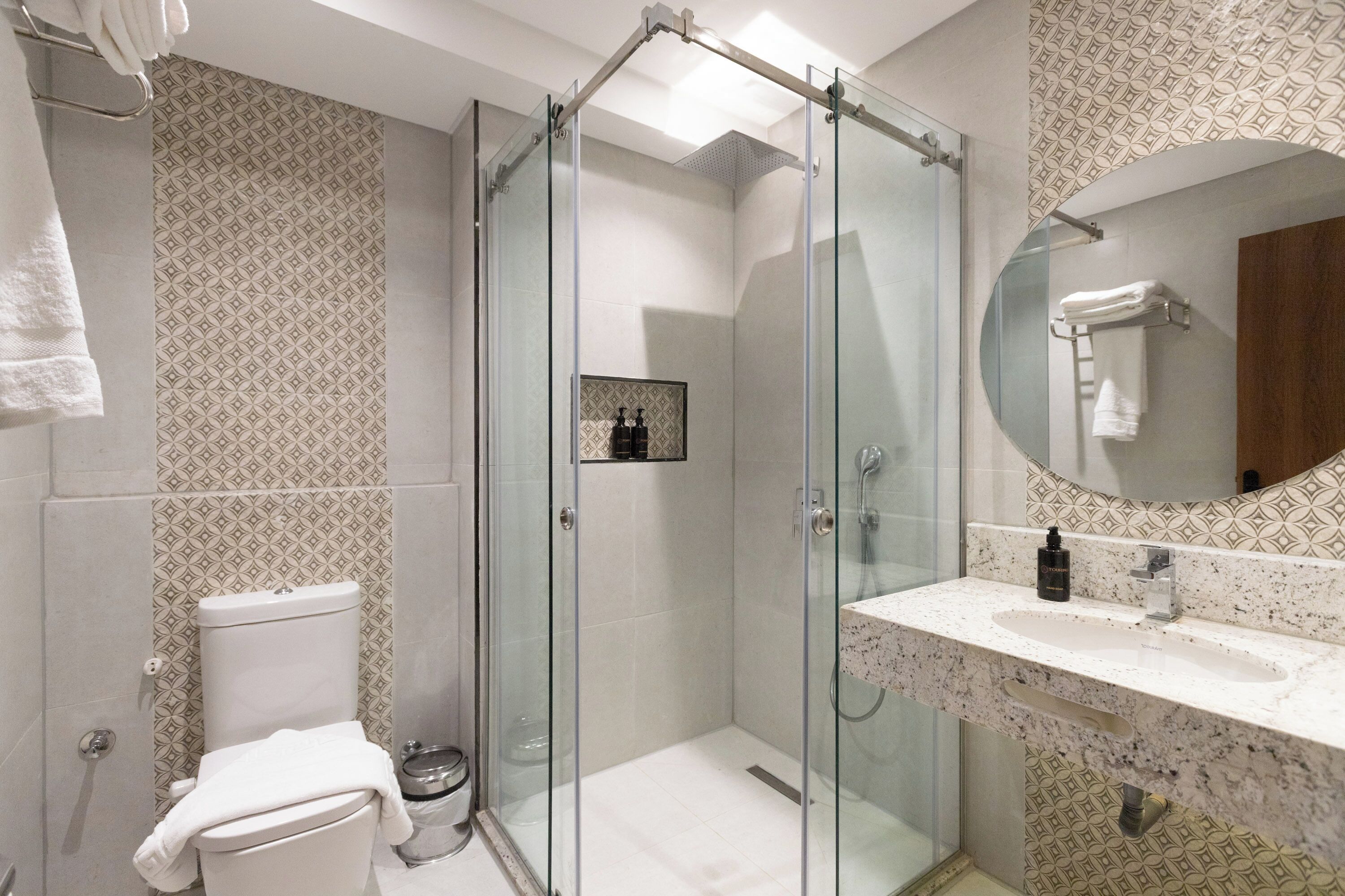 Un baño moderno con cabina de ducha de vidrio, inodoro y lavamanos con encimera de mármol.