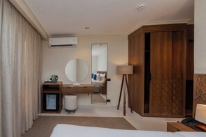 A hotel room with a bed, a desk with a mirror, a wardrobe, a small fridge, and a bedside table with a lamp. - Touring Pyramids Hotel (Giza)