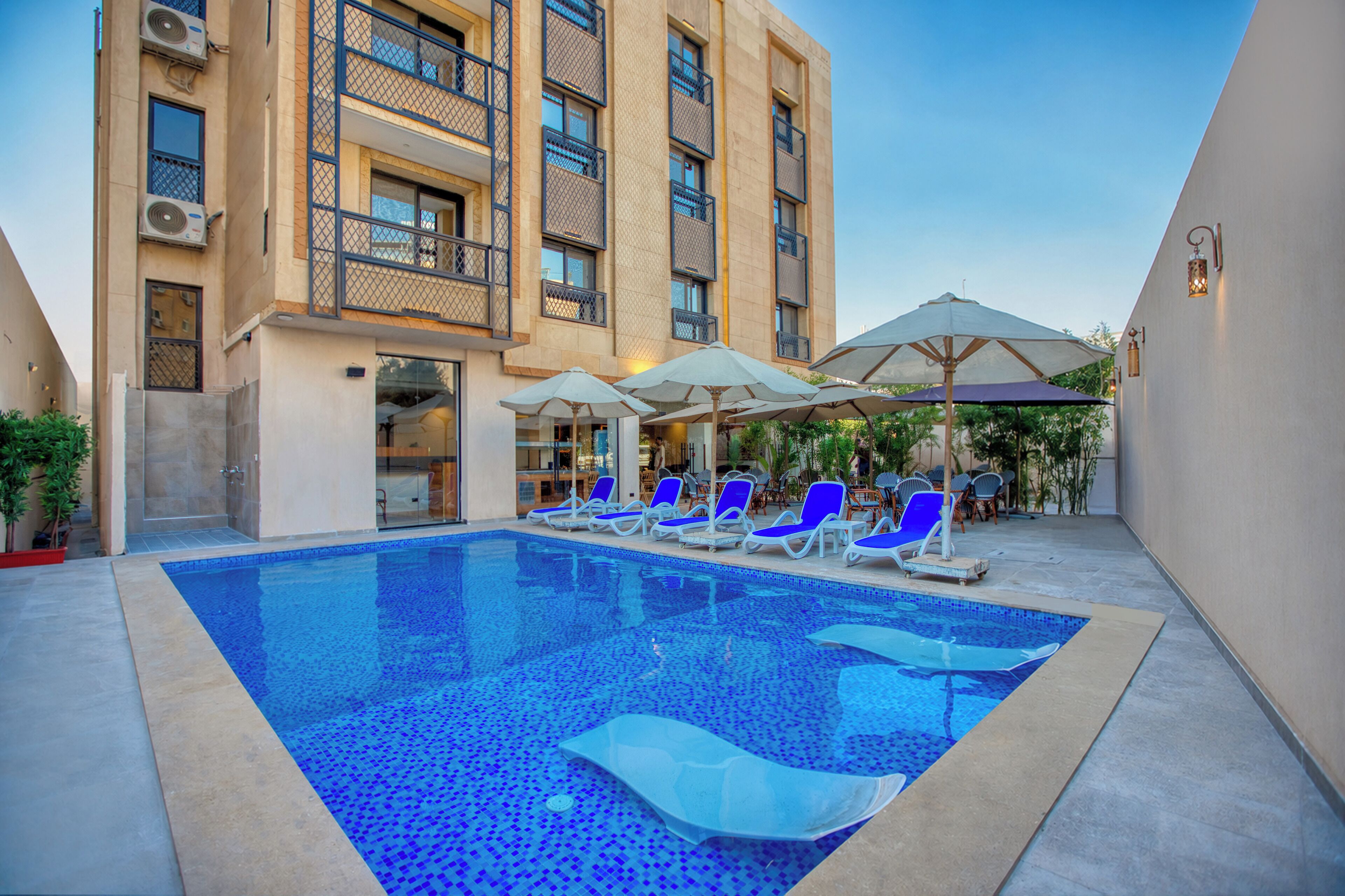 A swimming pool with lounge chairs and umbrellas, surrounded by a building with balconies.