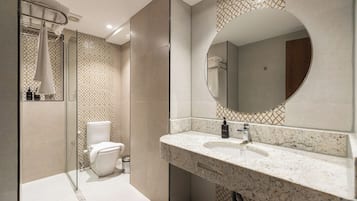 A modern bathroom with a glass shower enclosure, a toilet, a sink with a marble countertop, and a large mirror.
