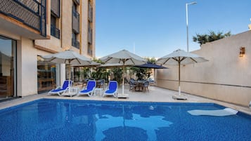 A swimming pool with lounge chairs and umbrellas, surrounded by a building with a modern design.