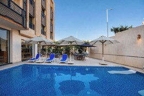 A swimming pool with lounge chairs and umbrellas, surrounded by a building with a modern design. - Touring Pyramids Hotel (Giza)