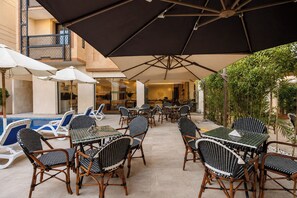 An outdoor seating area with wicker chairs and tables, umbrellas, and a pool in the background. - Touring Pyramids Hotel (Giza)