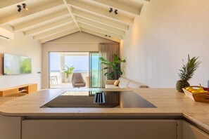 A modern kitchen with a central island, a dining area with a sofa and chairs, and a view of the outdoors. - Azzurro at The Reef Ocean View Penthouse (Sint Michiel)