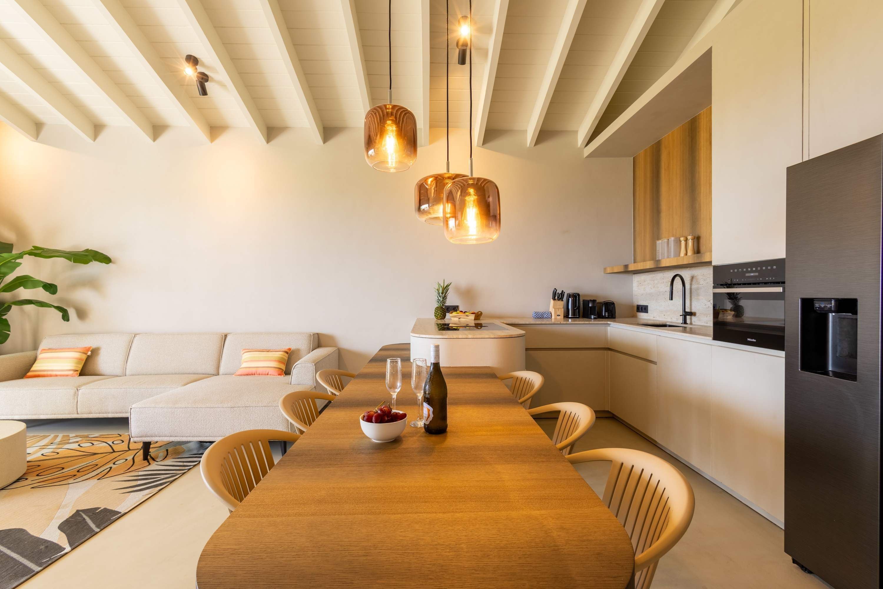 A modern kitchen with a dining area, featuring a wooden table, chairs, and pendant lights.