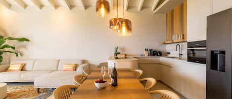 A modern kitchen with a dining area, featuring a wooden table, chairs, and pendant lights.