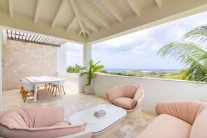 A covered outdoor seating area with a table and chairs, a potted plant, and a view of the landscape. - Azzurro at The Reef Ocean View Penthouse (Sint Michiel)
