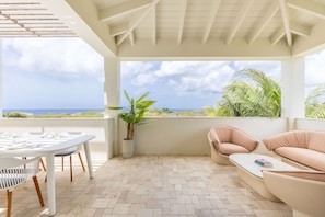 A covered outdoor seating area with a table and chairs, a potted plant, and a view of the ocean. - Azzurro at The Reef Ocean View Penthouse (Sint Michiel)