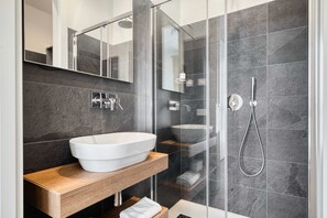 A modern bathroom with a large white sink, a glass shower enclosure, and dark marble walls. - w Pleasant 1BR Near Milan City Center (Milan)