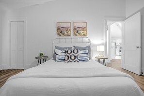 Un dormitorio con una cama grande, dos mesitas de noche, una lámpara y dos cuadros en la pared.