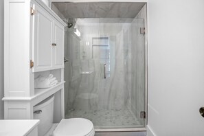 Un baño moderno con cabina de ducha de vidrio, muebles blancos y un inodoro.