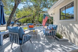 Eine Holzterrasse mit Gartenmöbeln, einer amerikanischen Flagge und Blick auf ein Haus.
