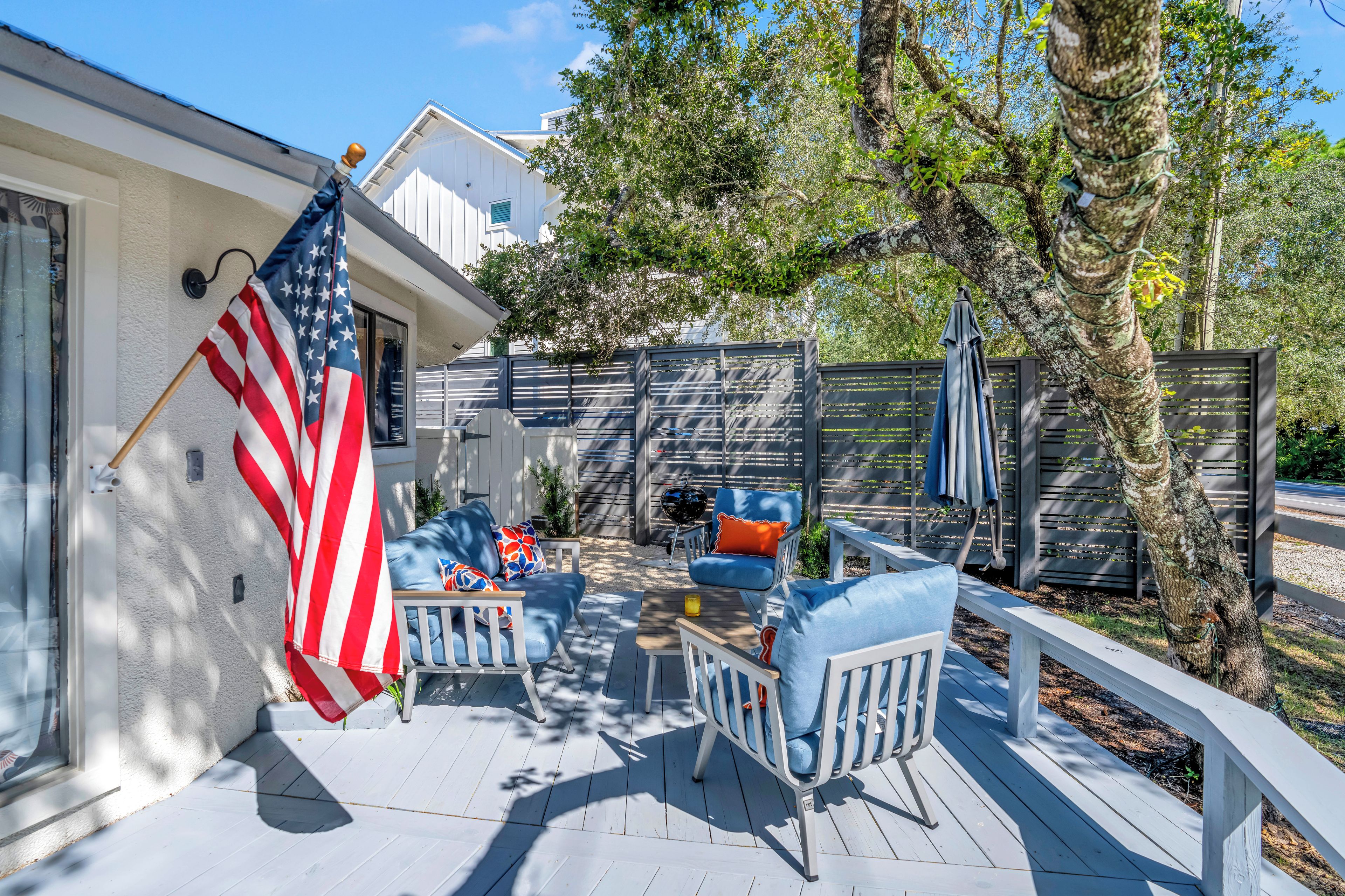 Une terrasse extérieure couverte, avec des meubles blancs, un drapeau et une clôture en bois.