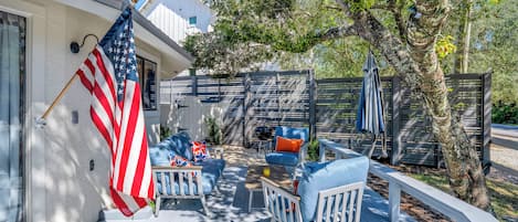 Une terrasse extérieure couverte, avec des meubles blancs, un drapeau et une clôture en bois.