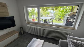 Ein Zimmer mit großem Fenster, Flachbildfernseher, Heizkörper und einer Couch.