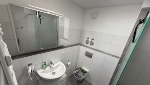 Un baño moderno con cabina de ducha de vidrio, un lavamanos blanco con un espejo encima y un inodoro con función bidé.