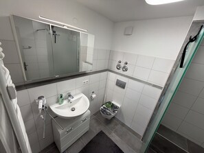 Un baño moderno con cabina de ducha de vidrio, un lavamanos blanco con un espejo encima y un inodoro con función bidé.
