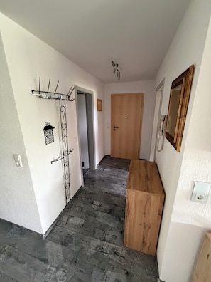 A hallway with a wooden door, a coat rack, and a mirror on the wall.