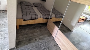 Una habitación pequeña con cama, un estante y un espejo.
