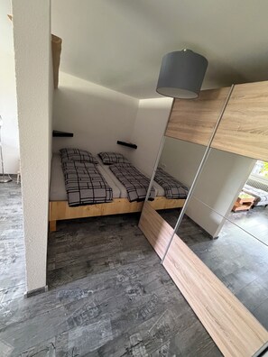 Una habitación pequeña con cama, un estante y un espejo.
