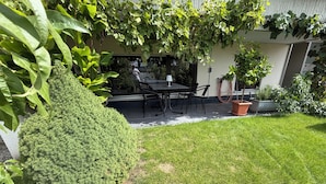 Un patio cuidado con una mesa y sillas, rodeado de abundante vegetación y un seto bien recortado.