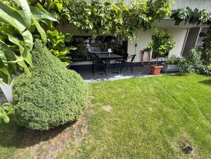 Un patio cuidado con una mesa y sillas, rodeado de abundante vegetación y un seto bien recortado.