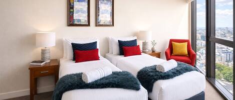 A hotel room with two beds, a red chair, a large window, and two framed pictures on the wall.