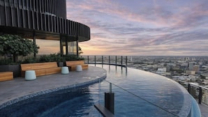 A rooftop infinity pool with a city view, wooden seating, and a modern building structure. - Sky-high Haven-rooftop Infinity Pool Parking Wifi (Brisbane)