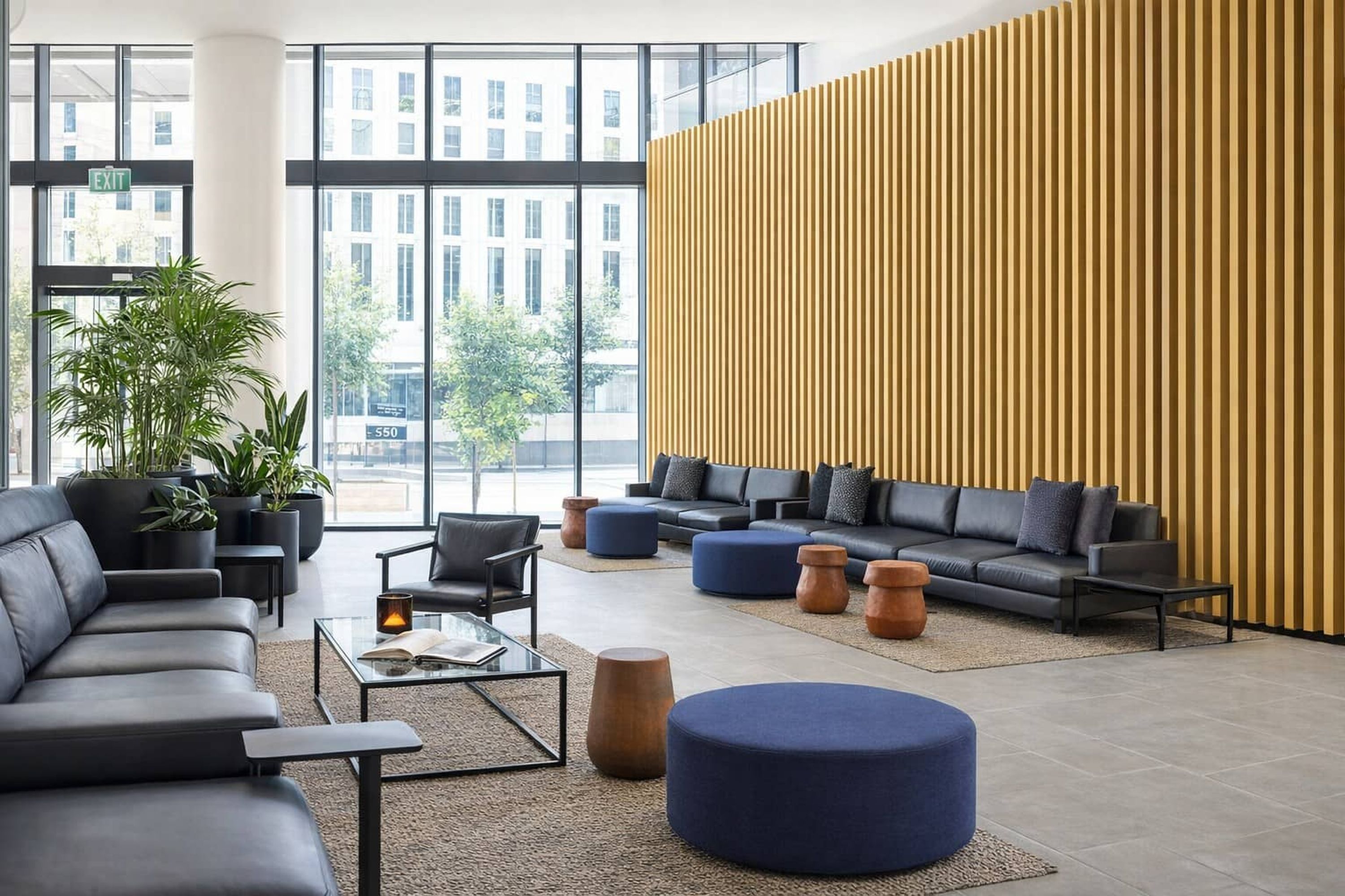 A modern lobby with leather sofas, a glass coffee table, potted plants, and a large window offering a city view.