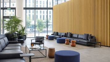 A modern lobby with leather sofas, a glass coffee table, potted plants, and a large window offering a city view.