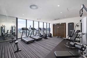 Une salle de sport moderne équipée de tapis de course, de machines de musculation et offrant une vue sur la ville.