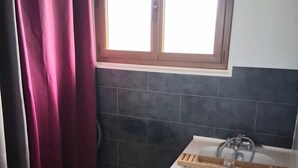 Ein Badezimmer mit einer Badewanne, einem Fenster mit Vorhängen und dunkel gefliesten Wänden.