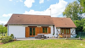 Eingeschossiges Haus mit Ziegeldach, einer Veranda mit Gartenmöbeln und einer kleinen Gartenanlage.